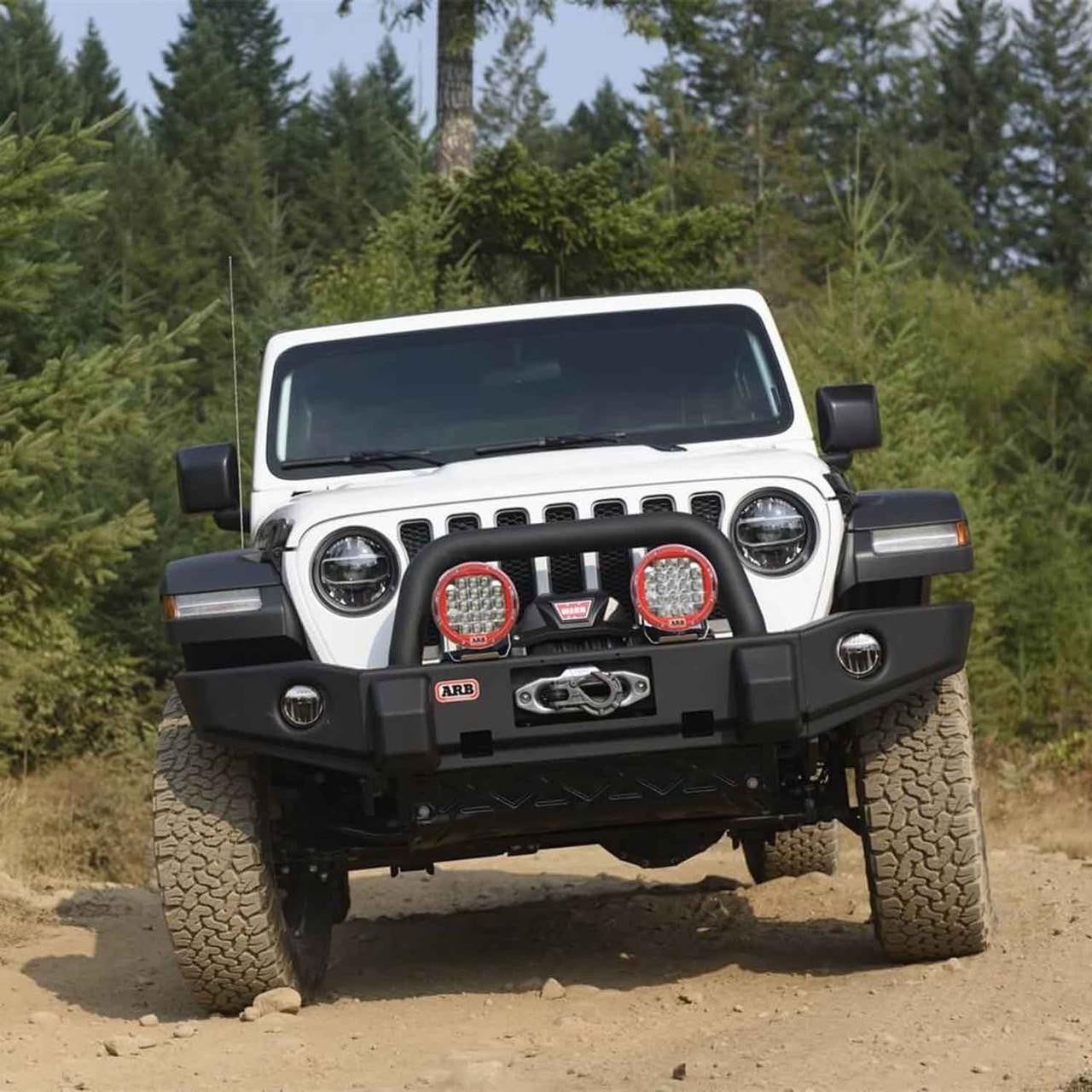 White Jeep Wrangler with additional lights on a dirt road surrounded by trees
