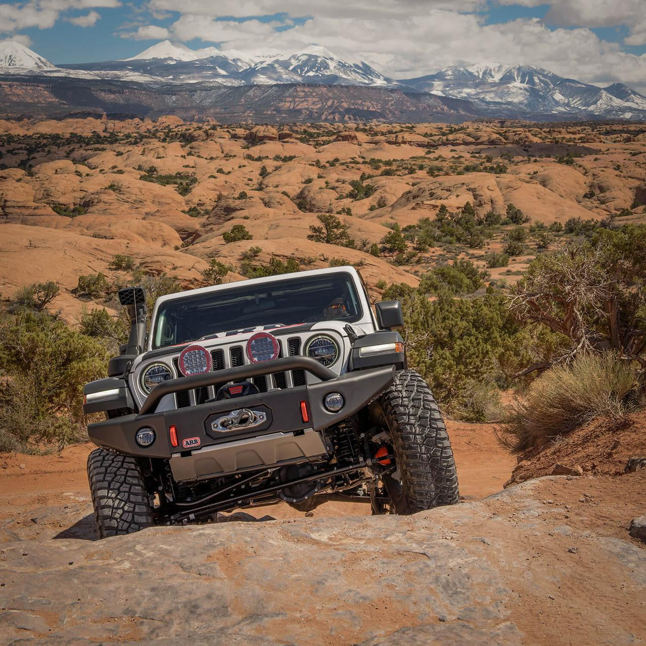 Jeep Wrangler on a rocky trail with desert landscape and mountains in the background