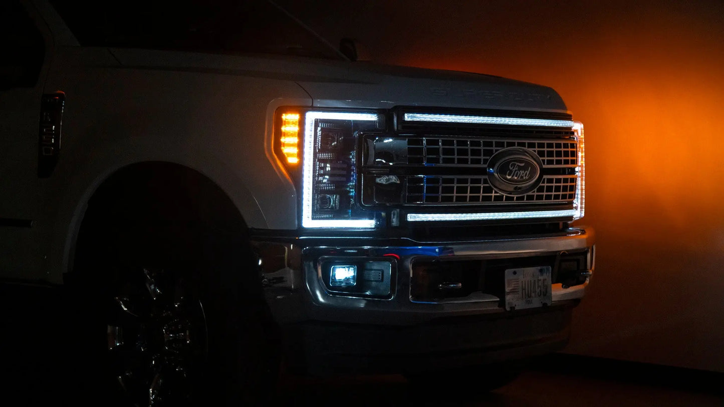 Front view of a white Ford truck with illuminated headlights and grille in a dark setting.