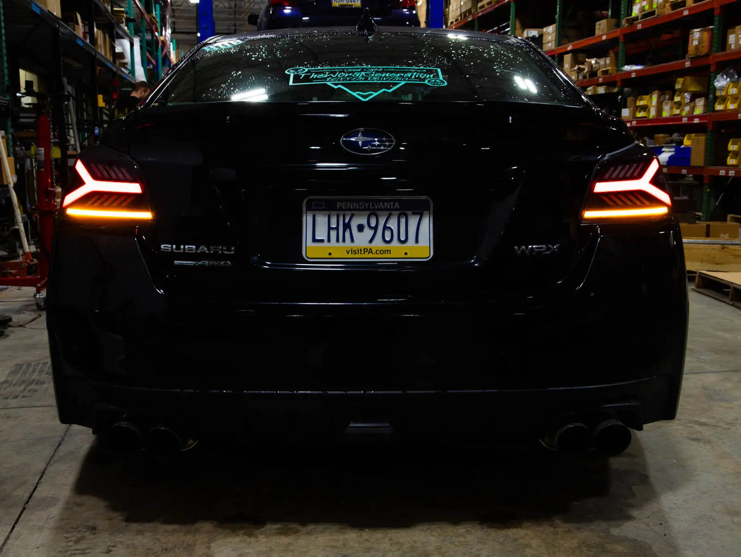 Black Subaru car with illuminated taillights in a warehouse setting