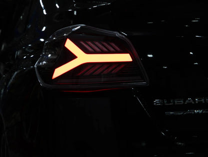 Close-up of a car's taillight with a distinctive logo on a dark background, featuring the brand 'Subaru'.